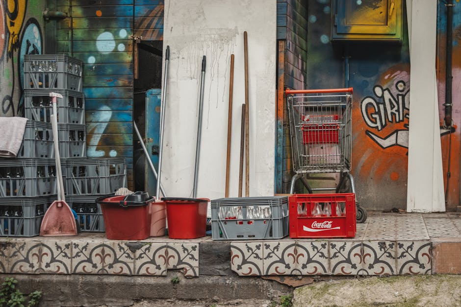 A collection of cleaning supplies and crates set against an artistic, graffiti-covered wall.